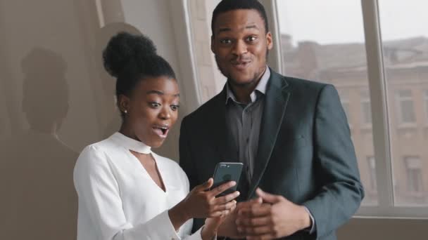 Genç ve heyecanlı Afrikalı meslektaşlar akıllı telefon ekranına bakıyor, mobil online bahis uygulaması kazananı ile coşkulu bir mutluluk hissediyorlar. İş kadını ve işadamı iyi haber zafer kavramını kutladılar — Stok video
