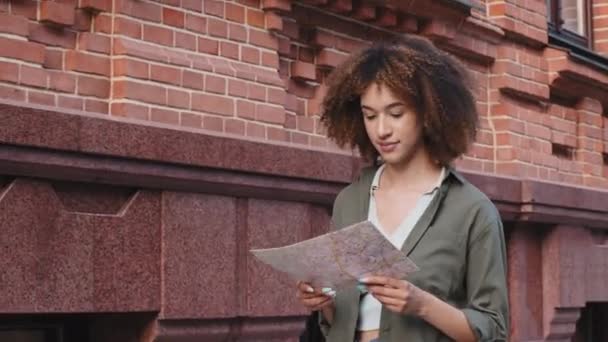Afro-Amerikalı kız şehir merkezinde elinde kağıt haritayla kaybolmuş görünüyor. Karışık ırk turisti, kıvırcık kadın blogcu ünlü mimari simgeler için kılavuz kitabı kullanıyor. Yaşam tarzı sırt çantası seyahat kavramı — Stok video