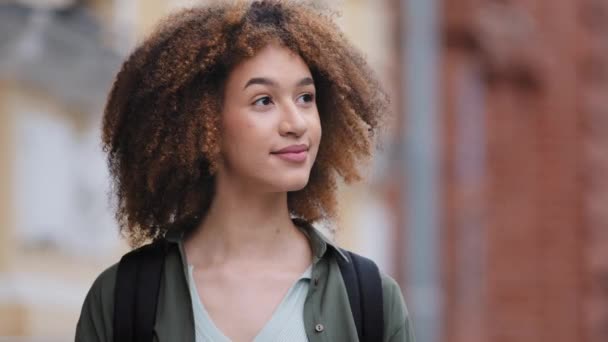 Attractive pensive curly African American girl tourist looking away distance outdoors. Pretty mixed-race black lady arriving in big city searches building, admires architecture. Summer travel concept — Stock Video