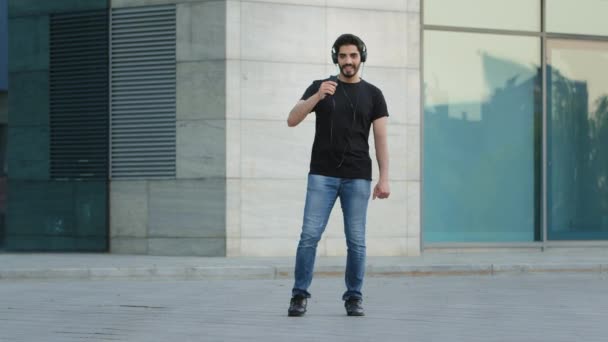 Vicces pozitív szakállas indiai arab férfi táncol a szabadban egyedül, mozog a kedvenc popzene ünneplő teljesítmény vagy hétvégén, gondtalan sötét hajú jóképű srác szórakozás szabadidő — Stock videók
