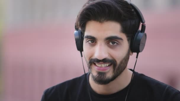 Heureux barbu jeune homme arabe indien portant des écouteurs profiter de la musique, souriant aux cheveux foncés Moyen-Orient excité étudiant masculin dans les écouteurs danser écouter des pistes préférées nouveau succès populaire en ligne — Video