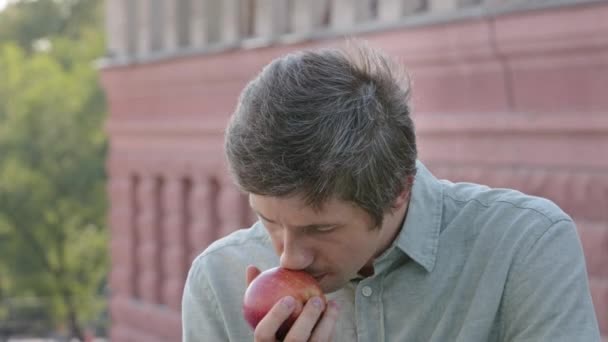 O vegan vegetariano masculino jovem mantém a bela maçã madura, inala o aroma delicioso. Dieta atraente cara desfrutando de café da manhã saudável vitamina ou almoço, cheirando frutas perfumadas, fechando os olhos admiravelmente — Vídeo de Stock