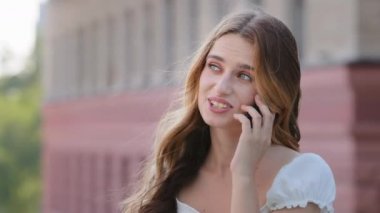 Gülümseyen milenyum kadını açık havada konuşmaktan zevk alıyor, mutlu genç kız cep telefonunu tutuyor cevap veriyor, çekici genç kız arkadaşıyla cep telefonuyla sohbet ediyor.