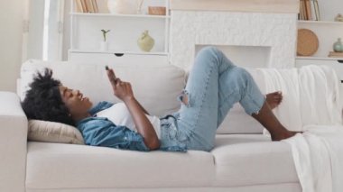 Tembel, gülümseyen Afrikalı genç bir kadın sosyal medyada sörf yapıyor, uygulamadan alışveriş yapıyor, mobil oyun oynuyor, yeni akıllı telefonlara mesaj atıyor. Rahat, dingin bir milenyum kadını kanepede uzanıyor, evde eğleniyor.