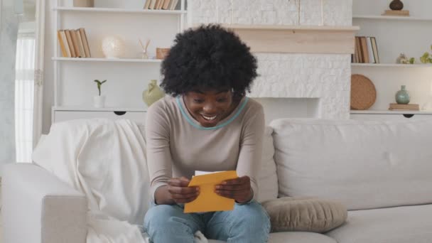 Heureuse excitée jeune femme afro-américaine enveloppe ouverte lit de bonnes nouvelles dans la lettre d'admission sur papier se trouve sur le canapé à la maison. Fatigué dame tenant avis postal obtenir remboursement de la taxe sur les bourses d'études ou salaire nouvel emploi — Video