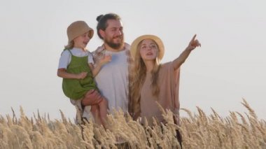Küçük kızı sakallı, sarışın bir adam, annesi ve çocuğu buğday tarlasına bakan anne ve babası olan mutlu, beyaz bir aile babası var.