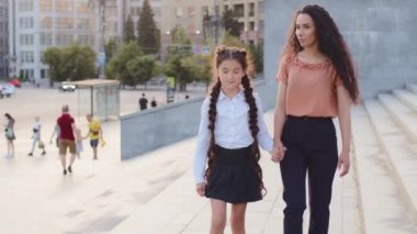 Genç kadın anne ve küçük liseli kız el ele tutuşup şehirde yürürken gülümsüyorlar. İspanyol ailesi okula gidiyor. Anne, bekar ebeveyn kızı derse götürüyor.