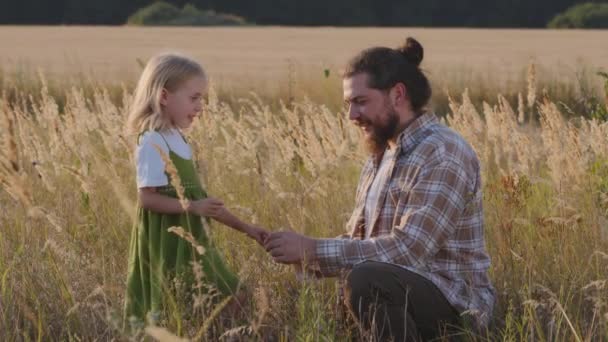 Cuidar papá caucásico barbudo hombre papá adulto padre en campo de trigo toma de la mano niño pequeña hija niña niño hablando explicando conversación sonrisa pasar tiempo juntos al aire libre en la naturaleza hablar — Vídeo de stock