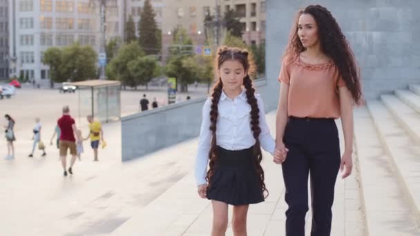 Genç kadın anne ve küçük liseli kız el ele tutuşup şehirde yürürken gülümsüyorlar. İspanyol ailesi okula gidiyor. Anne, bekar ebeveyn kızı derse götürüyor. — Stok video