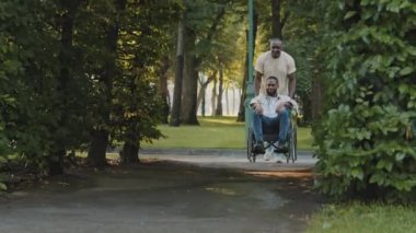 İki kaygısız Afrikalı Amerikalı yaz parkında fıskiyelerin önünden geçiyor. Olgun yetişkin siyah adam tekerlekli sandalyedeki genç sakallı adamı itiyor. Engelli kişi hafta sonları dışarıda yürümekten hoşlanıyor