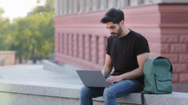 Bıyıklı genç Hintli sakallı adam modern laptop klavyesinde yazı yazıyor, ortadoğulu erkek çalışan dışarıda bilgisayar çalışıyor, müşteriye danışıyor ya da internetten ders çalışıyor, teknoloji kavramı.
