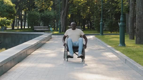 Orang Afrika-Amerika penyandang cacat menggunakan kedua tangan di kursi roda aktif. Pria kulit hitam dewasa cacat berjalan sendirian di taman tanpa ditemani. Konsep lingkungan yang dapat diakses — Stok Video