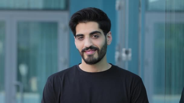 Молодий індійський арабський студент або бізнесмен з вусами і бородою придивляється до фотоапарата на вулиці. Посмішка середнього сходу тисячоліття з чорним волоссям в літній футболці задоволені клієнтом, клієнт — стокове відео