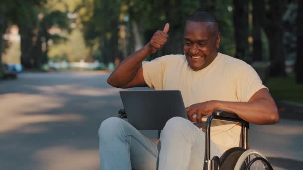 Homme adulte adulte paralysé afro-américain utilisant un ordinateur portable a reçu de bonnes nouvelles, e-mail, offre d'emploi ou de compensation. Une personne handicapée noire en fauteuil roulant se réjouit de célébrer la victoire, la victoire de loterie, le succès — Video