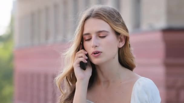 Frustrovaný rozzlobený tisíciletá žena mluví po telefonu venku, rozhořčený mladý dívka drží mobilní telefon při zvedání hovoru, atraktivní blondýny dáma s nepříjemnou konverzaci od mobilu s přítelem — Stock video