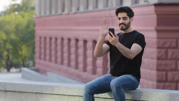 Sorrindo jovem indiano árabe homem olhar para a tela do smartphone falar sobre chamada de vídeo no gadget moderno. Happy millennial Oriente Médio cliente masculino ou usuário tem webcam conferência virtual digital no celular — Vídeo de Stock