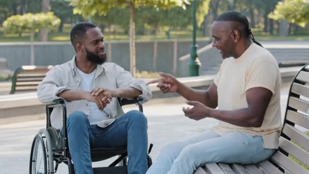 Joven barbudo negro discapacitado en silla de ruedas gestos emocionalmente, hablar de negocios con un colega senior, pareja o amigo. Dos hombres afroamericanos dan la mano celebran la cooperación inicial — Vídeo de stock