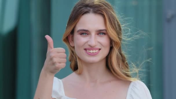 Porträtt av glad ung säker europeisk kaukasisk kvinna stå utomhus titta på kameran rekommenderar god service, leende vit hud frisk tusenårig flicka poserar visa tummen upp ge rekommendation — Stockvideo