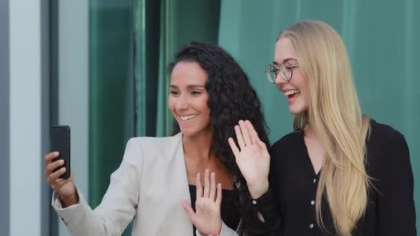 Självsäkra olika affärskvinnor chatta med kollega med hjälp av smartphone utomhus, leende multiracial millennial kvinnliga medarbetare tittar på skärmen, anställda briefing, studenter brainstorming online — Stockvideo