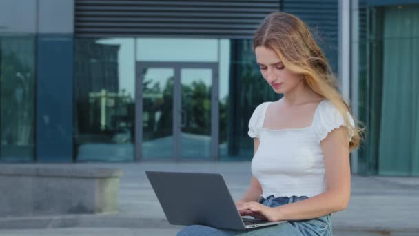 Serious young blonde European lady writing blog or chatting with friends in social network. Focused attractive Caucasian Scandinavian woman freelancer working online using laptop, typing outdoor — Stock Video