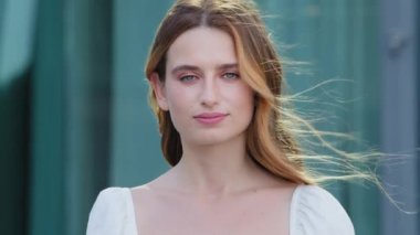 Sakin, güzel, sağlıklı bir milenyum kadını, dışarıda kameraya bakıyor. Gülümseyen beyaz tenli, beyaz tenli, çekici yüzlü, kendine güvenen, yakın plan portre pozu veren yetişkin bir kız.
