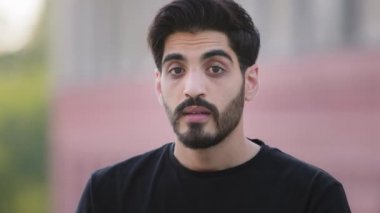 Korkak, orta doğulu sakallı, siyah tişörtlü genç adam korkmuş, korkmuş, Hintli erkek öğrenci gözlerini kapatmış ya da korkmuş, parmaklarından kötü şeyler görmekten kaçınıyor.