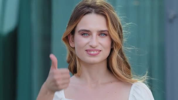 若い満足したドイツ北欧の女性の白い歯をカメラを見て親指を示す笑顔。幸せな白い肌のヨーロッパの女の子の学生のような歯科矯正サービスの概念をお勧めします — ストック動画