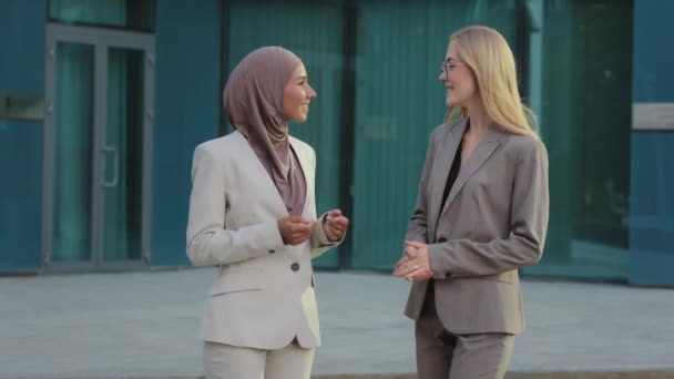 Multie-etnische vrouwelijke collega 's bespreken verslag buiten. Gelukkige zakenvrouwen in kantoorpakken en hijab die buiten staan, praten en gebaren. Multicultureel business team divers teamgenoten concept — Stockvideo