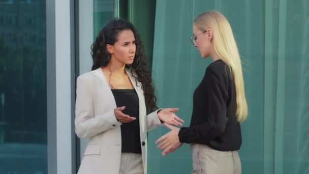 Deux collègues féminines sérieuses et diversifiées discutent près d'un immeuble de bureaux moderne, une femme d'affaires indienne a une conversation d'affaires avec un collègue caucasien discute de la réunion de travail du projet à l'extérieur — Video