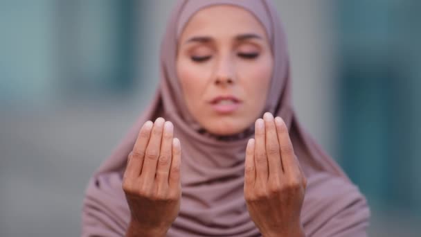 Κοντινό πλάνο θηλυκό πρόσωπο σοβαρή μουσουλμάνα γυναίκα φοράει μπεζ μαντίλα παραδοσιακή ενδυμασία προσεύχεται σε εξωτερικούς χώρους στην πόλη για τον Αλλάχ. Θρησκευτικό ισλαμικό αραβικό κορίτσι προσεύχονται με τα χέρια, κυρία λέει ψιθυρίζει προσευχή ευλογία — Αρχείο Βίντεο