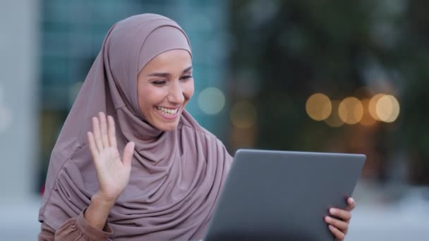 Musulmana joven islámica chica estudiante mujer de negocios vistiendo hijab sentado al aire libre haciendo videollamada remota en línea utilizando el ordenador portátil para la conferencia de chat con la familia saludando de la mano hablando webcam — Vídeos de Stock