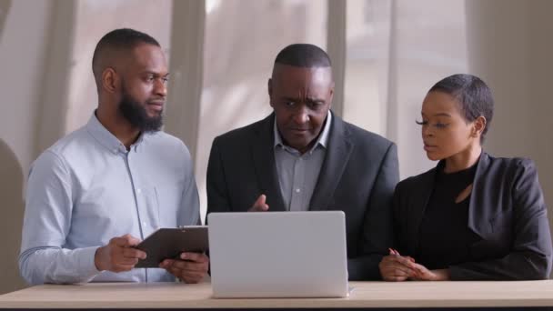 Sérieux bouleversé adulte africain homme d'affaires mature patron parle des erreurs dans le projet de démarrage à la femme gestionnaire et travailleur gars, trois partenaires afro discuter affaire assis à la table au bureau avec ordinateur portable — Video