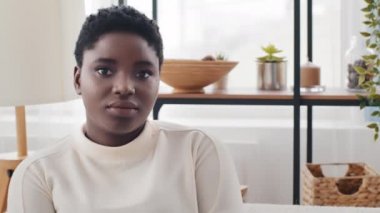 Güzel Afro-Amerikan sakin kız siyah afro kadın melez kadın evde oturmuş kameraya bakarken yüzünde barışçıl bir ifade vardı.