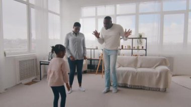 Afro-Amerikan aile eğlencesi hafta sonları evde eğleniyor, olgun siyah Afrikalı baba baba dansı ritmik hareketler gösteriyor anne ve küçük kız bebek gülüşmeleri