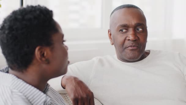 Afrikansk amerikansk par moden mand og afro ung pige kvinde sidder indendørs hjemme taler kommunikation tale dialog samtale tale dele ideer diskutere taler volleyball spil griner – Stock-video