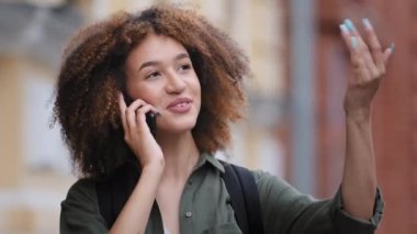 Açık havada duran Afrikalı etnik kökenli genç bir kadın telefonda hoş sohbetlerin tadını çıkarıyor. Haberleri ailenizle paylaşın, işi uzaktan çözün. Modern teknoloji ve mobil taşıyıcı bağlantı kullanımı kavramı