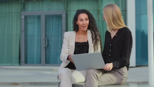 Feliz joven mujer de negocios caucásica utilizando el ordenador portátil con la risa mentor femenino al aire libre. Sonriendo diversas mujeres gerentes hablando de nuevo espectáculo de negocios ok gesto alegre buen concepto de noticias de la mañana — Vídeos de Stock