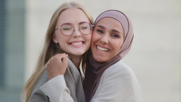Dwie szczęśliwe, uśmiechnięte młode kobiety, przyjaciółki lub koleżanki, przytulające się, szczęśliwe. Tysiącletnia Hinduska dziewczyna w hidżabie i młoda europejska blondynka razem. Feminizm, koncepcja stosunków międzynarodowych — Wideo stockowe
