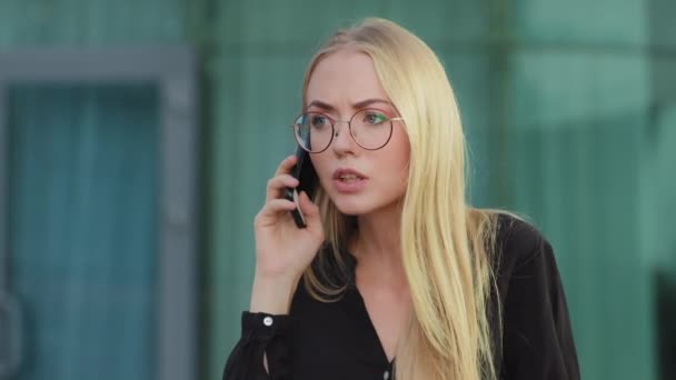Zaniepokojona, biała blondynka trzymająca telefon komórkowy wściekle rozmawiająca z bankiem na dworze. Klient niezadowolony z kiepskiej obsługi, wkurzony klient, agresywna koncepcja businesswoman — Wideo stockowe