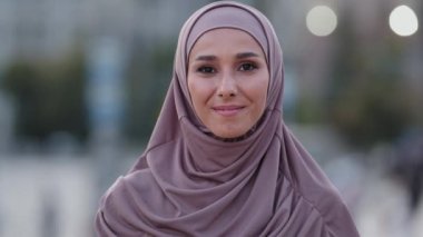 Yakın plan insan yüzü portresi müslüman genç arkadaş canlısı gülümseyen İslamcı kız yabancı müşteri tesettüre binyıllık Arap kadın takıyor açık havada kameranın dişlek gülüşüne bakıyor