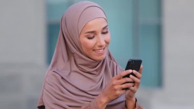 Açık havada kadın portresi İslami kız Müslüman genç kadın etnik kadın bej tesettür giyiyor geleneksel giysiler cep telefonu akıllı telefon sohbetleri yapıyor net bir mesajla gülümsüyor