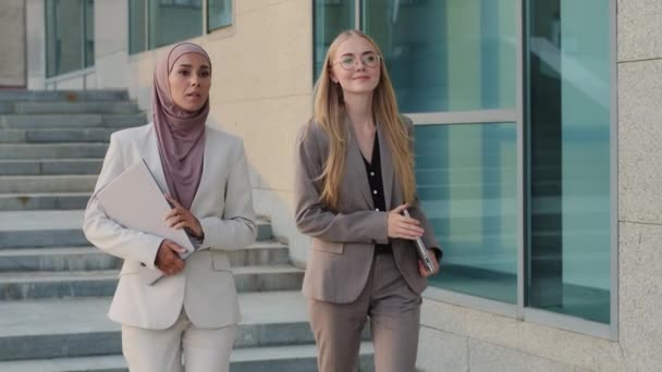 Con confianza sonriendo diversos colegas, chica india en hiyab y joven mujer eslava caucásica en ropa formal. Feliz propósito de las mujeres de negocios que descienden escaleras juntos. Concepto de moda empresarial para mujer — Vídeo de stock