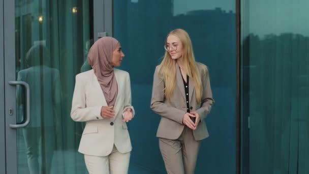 Chica india en hijab consulta con colega joven europea durante el descanso de la oficina. Diversas empresarias colegas caminando por la calle se comunican informalmente, discuten la próxima reunión o trato — Vídeos de Stock