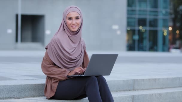 Úspěšná islámská dívka muslim mladá dospělá žena etnické ženy na volné noze podnikání student dáma nosí béžové hidžáb sedí na chodníku ve městě používá notebook pro práci na dálku prohlížení ukazuje ok gesto — Stock video