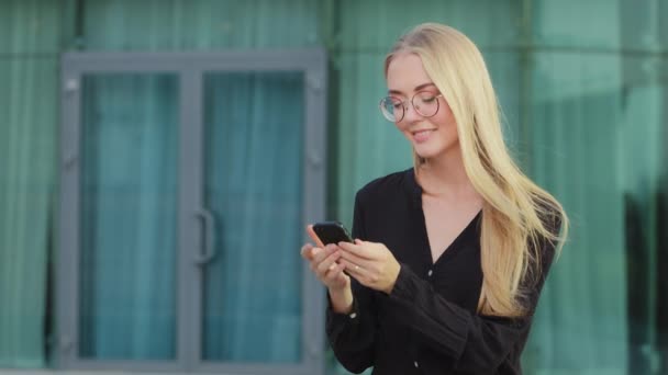 Wesoły biały student kobieta siedzi na zewnątrz blondynka młoda kobieta za pomocą telefonu, przerwa gospodarstwa telefon komórkowy surfing internet otrzymał wiadomość od znajomego na czacie o plany weekendowe — Wideo stockowe