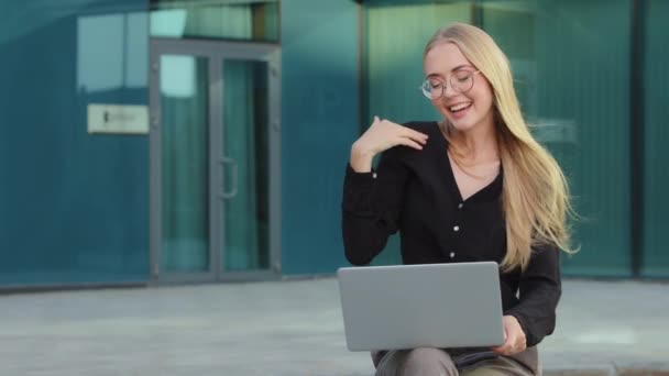 Menina millennial loira européia branca eufórica com óculos sentados ao ar livre usando laptop tem boas notícias. Jovem empresária ou freelancer se sentindo animada com a realização profissional — Vídeo de Stock