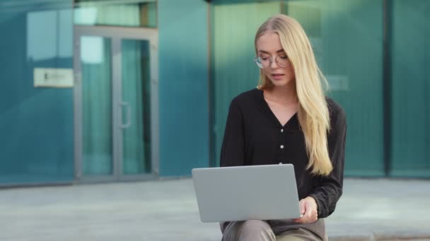 Mulher milenar pensativo em óculos olhar para a tela do laptop ao ar livre assistindo conferência on-line ou webinar, feminino jovem caucasiano pensativo em óculos de trabalho no computador, pense na solução do problema — Vídeo de Stock