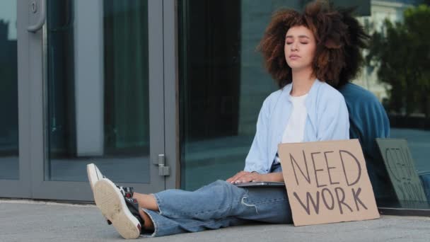 Smutne zdenerwowany afro amerykanka kobieta Afryki kręcone dziewczyna siedzi na chodniku w mieście przeciwko tła biurowiec firma z transparentem potrzebuje pracy stracona zwolniona pani bezrobotny problem kryzys — Wideo stockowe