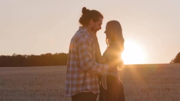 Sylwetki dwie osoby żonaty para rolnicy brodaty mężczyzna mąż chłopak i kobieta dziewczyna żona stoją w polu pszenicy n tło zachód słońca trzymając ręce rozmowy przytulanie czoło dotyk miłość — Wideo stockowe