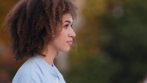 Cerca de mujer pensativo soñando cara joven hermosa chica esperando en la ciudad. Retrato al aire libre mujer afroamericana con el pelo rizado afro dama sentada al aire libre en el tiempo ventoso mirando hacia otro lado pensando — Vídeos de Stock